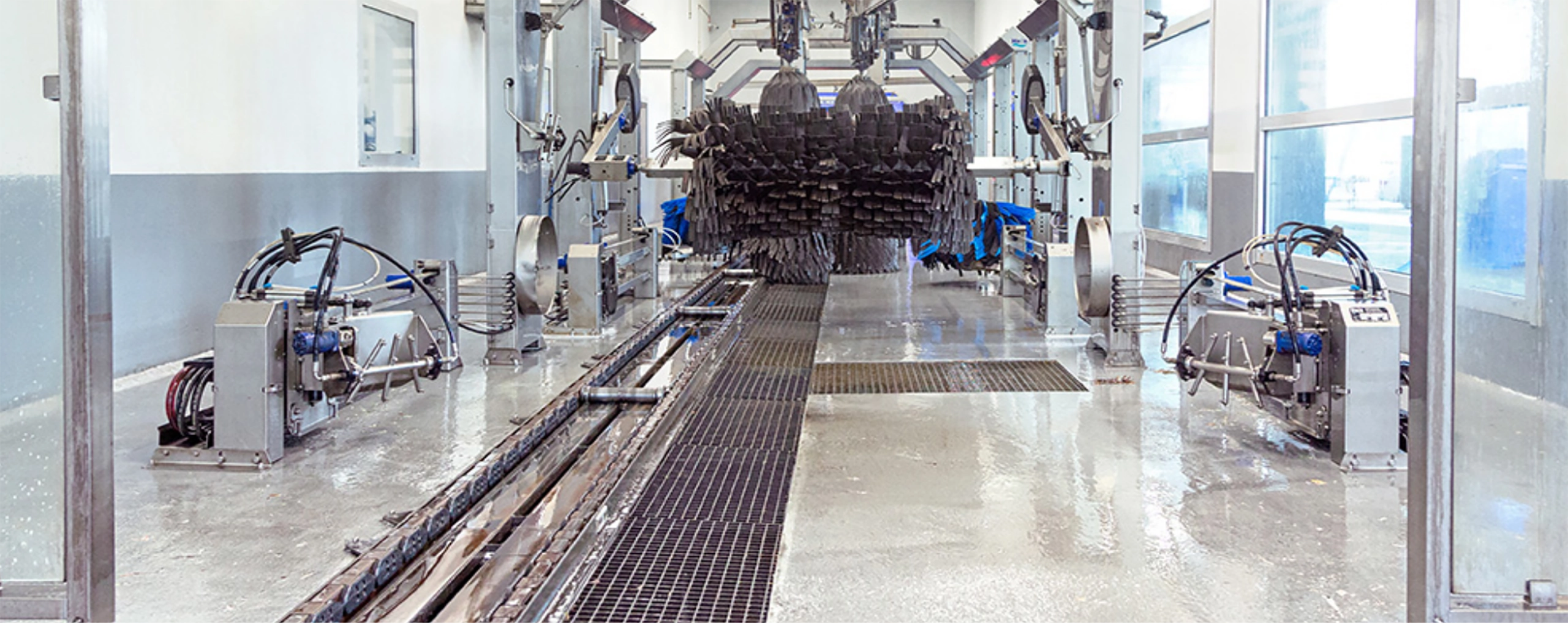 Automatisierte Waschanlage mit rotierenden Bürsten in hellem, industriellem Raum, ohne Personen.