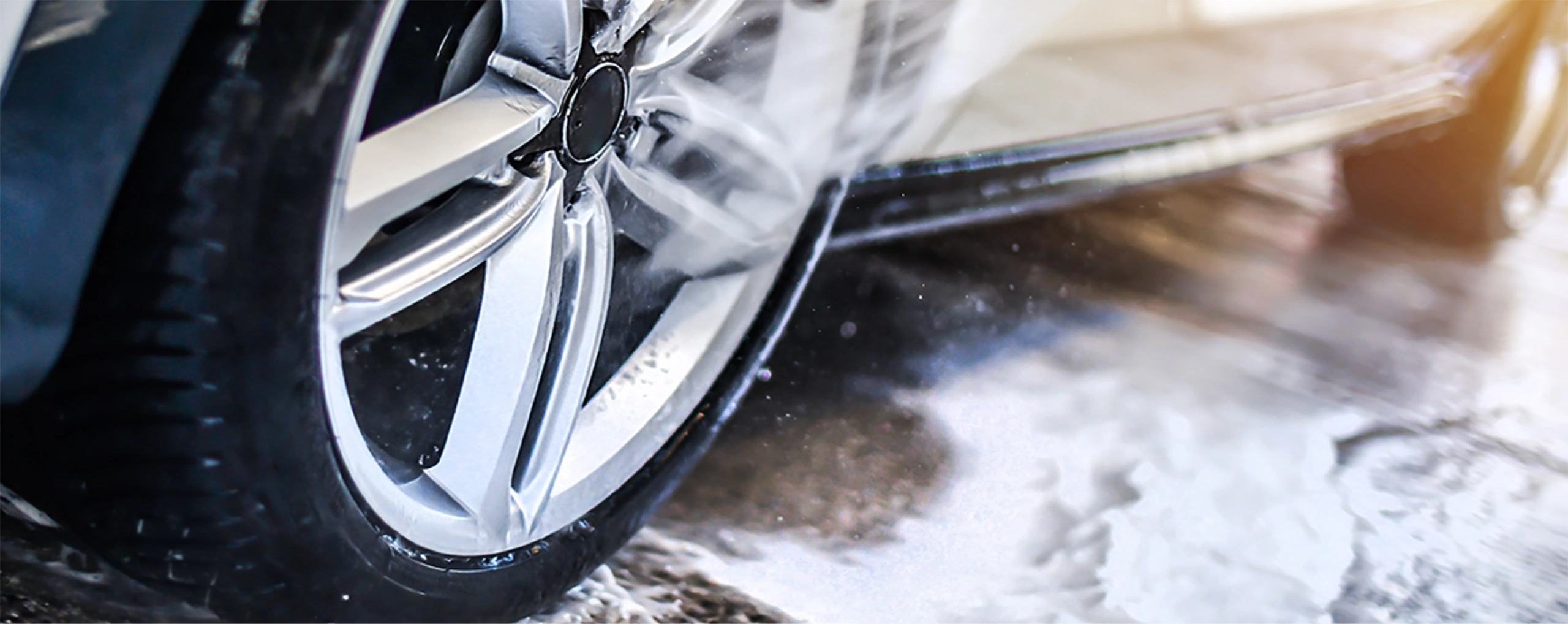 Autoreifen während der Autowäsche, mit Wasser und Schaum bespritzt. Felge glänzend und sauber.